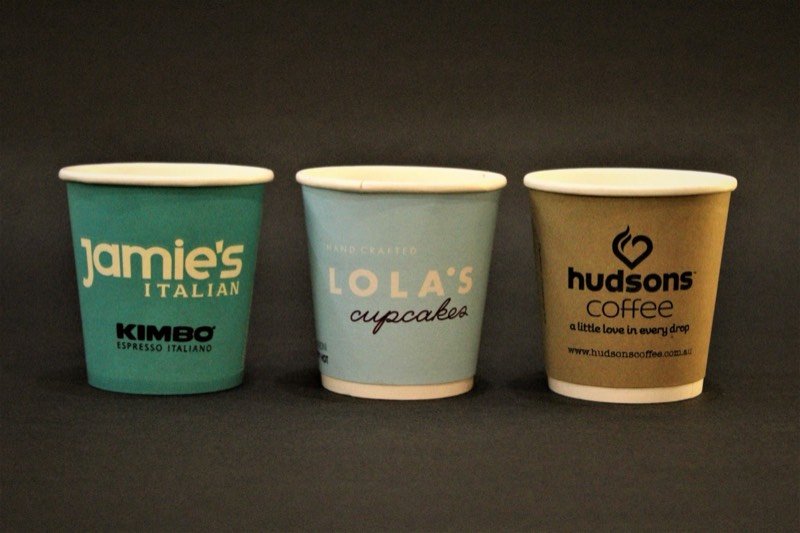 Three paper cups printed in different café brand liveries.
